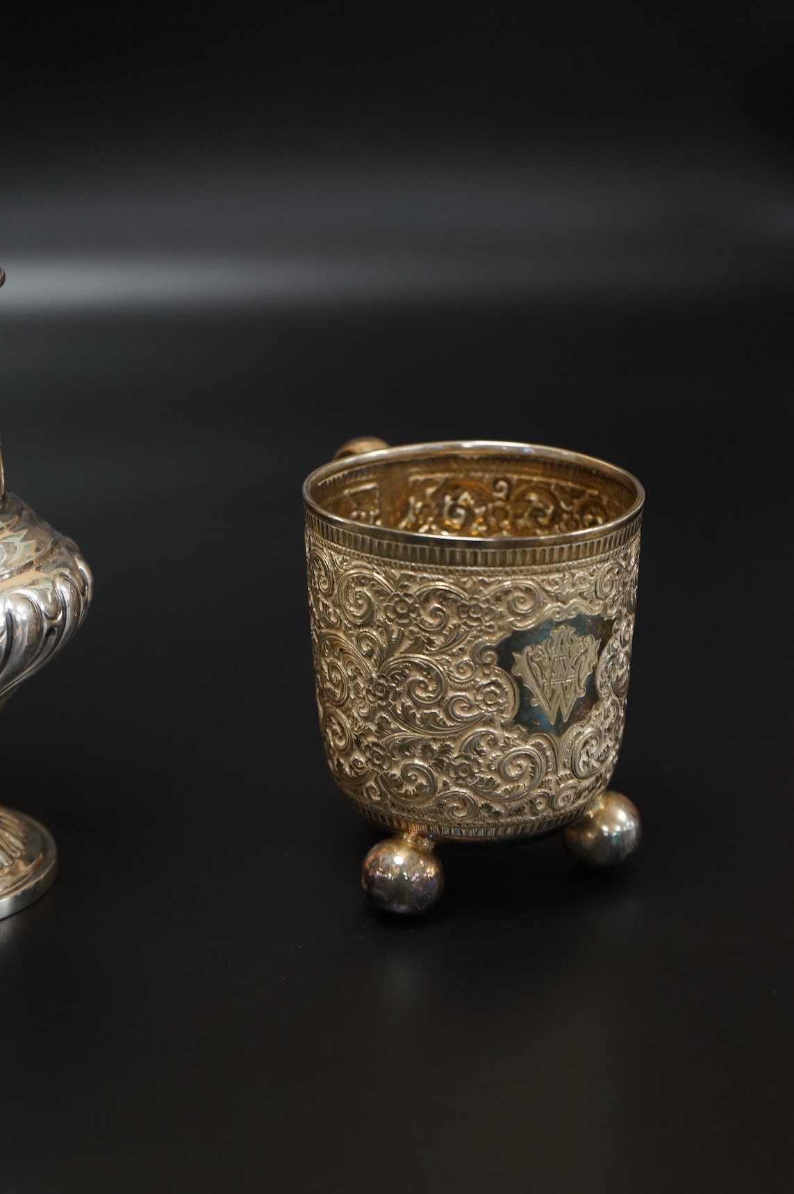 A Victorian embossed silver christening mug, on three ball feet, Martin, Hall & Co, London, 1874, height 85mm, together with a similar sugar caster, Lee & Wigful, Sheffield, 1899.